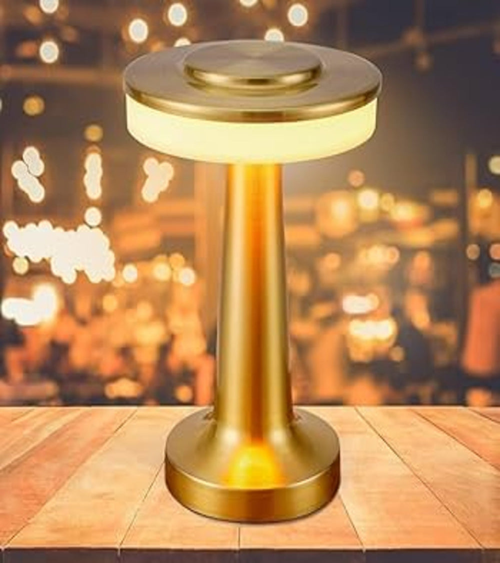 Modern golden rechargeable cordless table lamp glowing on a wooden table
