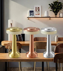 Set of three metallic portable LED lamps in gold, rose gold, and silver on a wooden table
